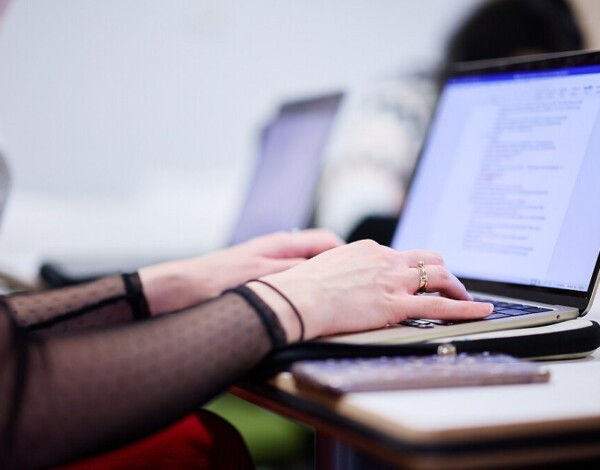 Person typing on a laptop in a classroom setting.