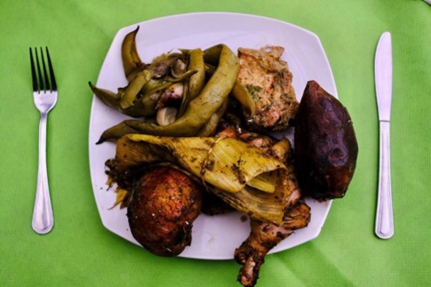 A plate of food including cooked meat and vegetables with a fork and knife laid either side of the plate on a green table.