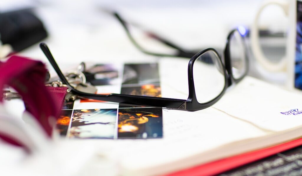 Black-framed eyeglasses on top of photographs and papers with a blurred background.