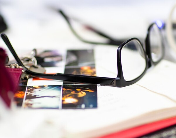 Black-framed eyeglasses on top of photographs and papers with a blurred background.