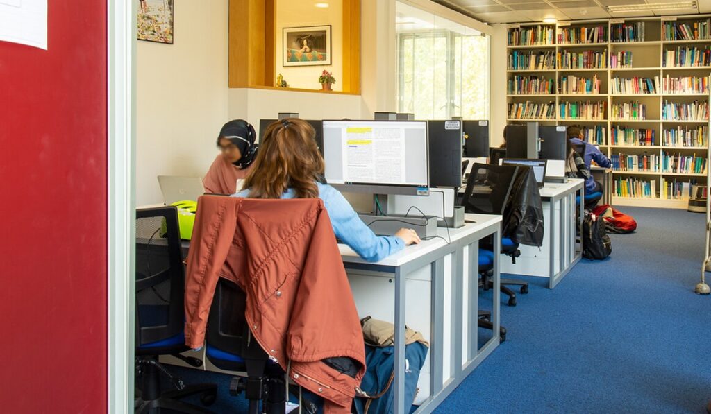 Students working at computer desks in a library with shelves full of books. Taken in ther UCL Great Ormond Street Institute of Child Health Library.