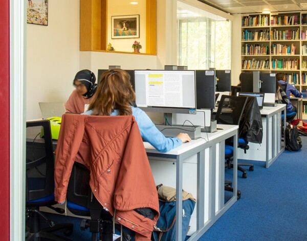 Students working at computer desks in a library with shelves full of books. Taken in ther UCL Great Ormond Street Institute of Child Health Library.