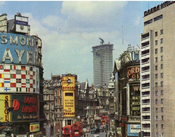 City street with double-decker buses, tall buildings with ads, and a high-rise tower in the background. This image is used on the cover of Anti-Atlas