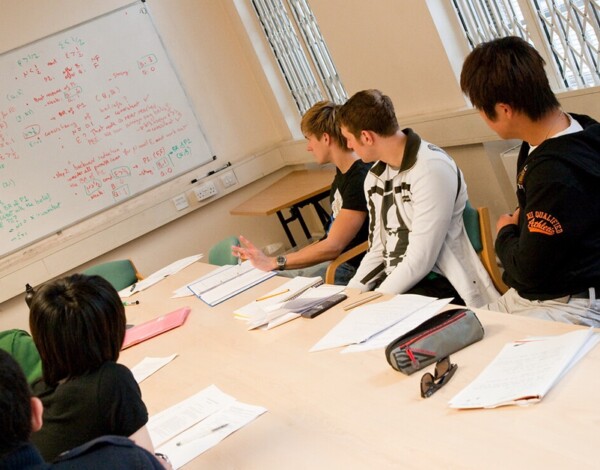 Students in a classroom watching a peer explain equations on a whiteboard.