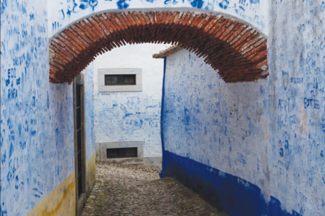 A narrow cobblestone alleyway with white walls covered in blue graffiti and a red brick archway overhead, as featured on the cover of New Sensory Approaches to the Past.