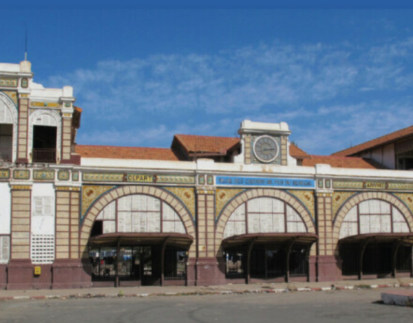 Exterior view of the Terminus Market in Dakar, showcasing ornamental arches, a clock, and a light blue shipping container in front.