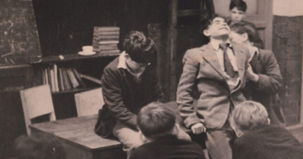 Black-and-white photograph of six people gathered in a rustic room, including a suited adult being kissed on the cheek and two children seen from behind.