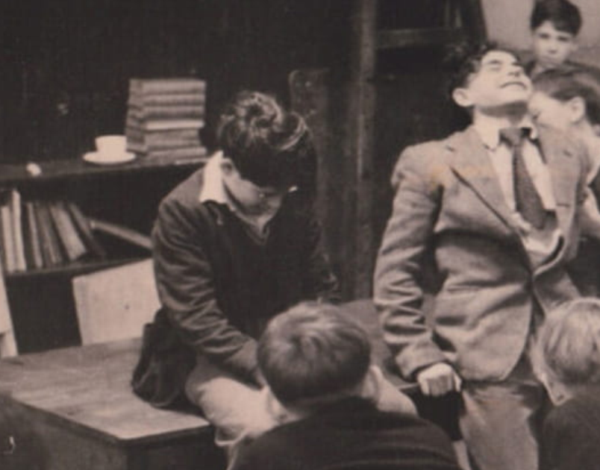 Black-and-white photograph of six people gathered in a rustic room, including a suited adult being kissed on the cheek and two children seen from behind.