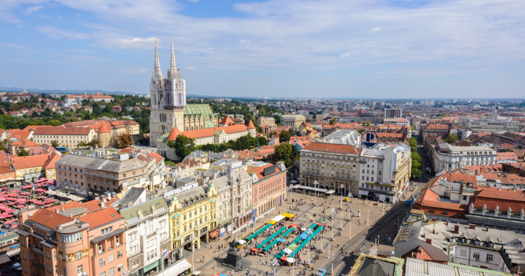 Elevated view of Zagreb Cathedral and Ban Jelačić Square, surrounded by colorful historic buildings and market stalls.