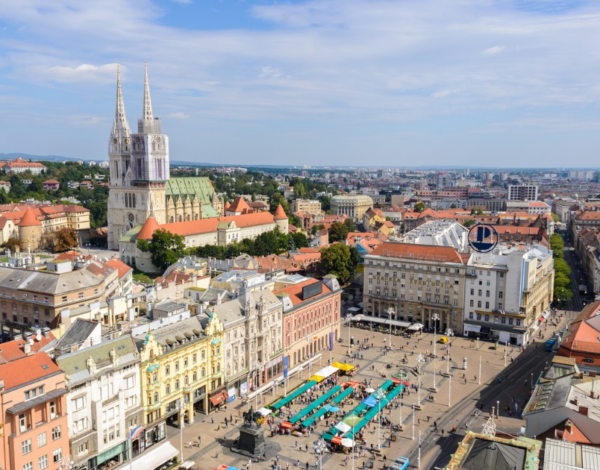 Elevated view of Zagreb Cathedral and Ban Jelačić Square, surrounded by colorful historic buildings and market stalls.
